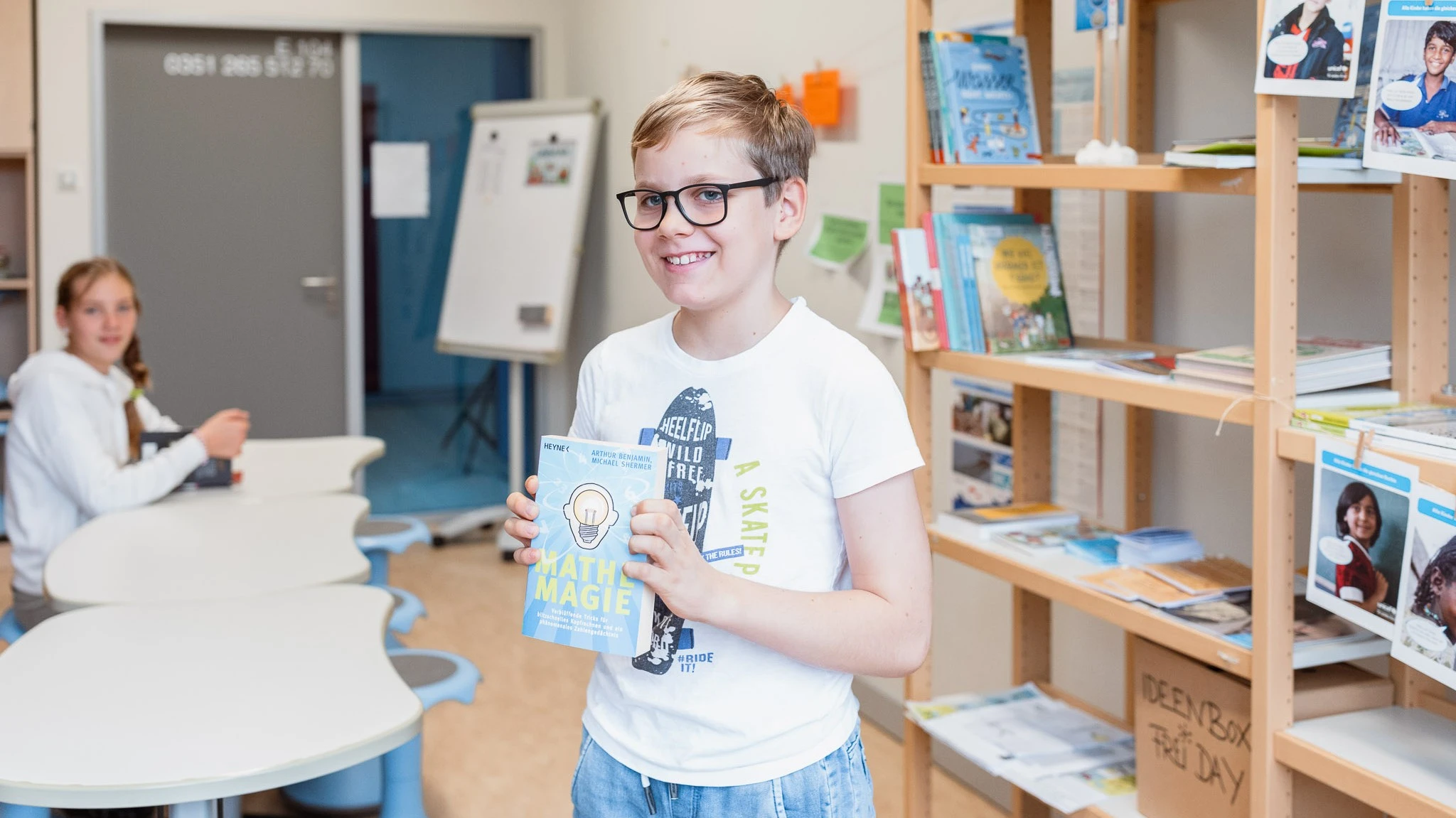 Schüler mit Buch vor Bücherregal
